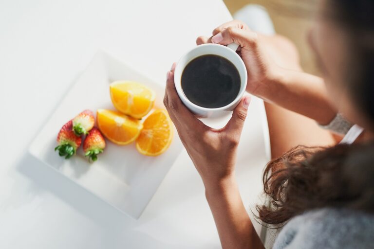 A person enjoying a cup of coffee with a bowl of cherries and fresh fruits.